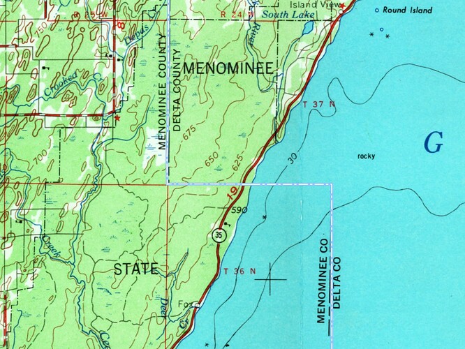 The Menominee–Delta county line in OHM follows the topographic basemap, heading north and west along a range line in T36N in Green Bay before turning north again along the range line between T37NR25W and T37NR24W.